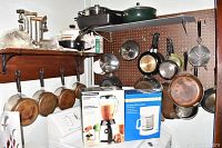 Full view of kitchen corner with boxed blender and coffee maker on washer, pans and pots hung on pegboard, and vintage meat grinders on wooden shelf.