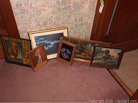 Photo showing multiple framed wall decor pieces arranged on floor against a wall with floral wallpaper, includes a vintage horse advertisement, dog print, water lilies, rural farm tractor, and countryside landscape prints.