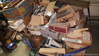 Overview of stacked boxes and tools on a dolly/cart showing a variety of labeled boxes and loose hand tools including tape dispensers and cables