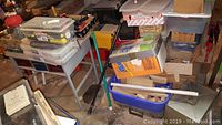Wide view of workshop area with tables, toolboxes, containers, and assorted items stacked and scattered in basement workshop.