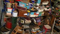 Photo of workshop items displayed on wooden shelves including labeled boxes, jars, and cans containing various hardware and tools unorganized