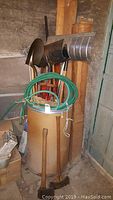 Full view of barrel filled with various yard tools including shovels, green hose coiled on top, axes and rakes grouped inside the barrel.