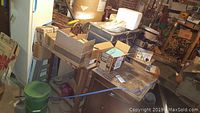 Overview of lot showing vintage wooden music cabinet, wooden table with boxes, old trunk, and various items in basement setting.