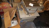Photo of Craftsman table saw showing metal cabinet and surface wear, placed in a basement space with some woodworking items around.