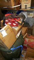 Red spool or cable reel with black handles resting on boxes, surrounded by stacked cardboard boxes and bins.