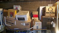 Overview photo showing multiple boxes stacked in basement including one labeled 'wheels' and other hardware items