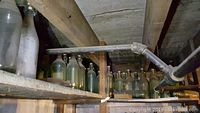 Shelf of over two dozen vintage glass home brewing bottles, varying sizes and colors, with stoppers attached.
