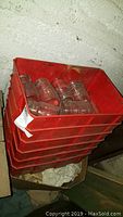 Stacked red plastic bins with glass canning jars inside against white wall.