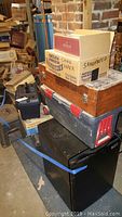 Stack of toolboxes and labeled boxes including 'Sandpaper' on top of mini fridge in basement area