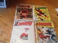 Four Daredevil comic books displayed on a wooden surface, showing front covers of issues 9, 83, 187, and 189.