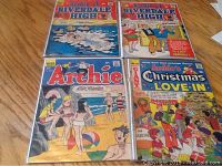Four Archie comics laid out on wood floor showing front cover artwork including two Riverdale High comics, one Archie comic, and one Christmas Love-In comic
