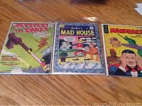 Three vintage comic books on a wooden surface: 'Mystery in Space' left, 'Archie's Mad House' center, and partial view of 'Mandrake the Magician' right.