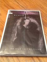 Photo of DC Death comic with title 'the high cost of living' showing a shadowed figure looking upward and a key symbol