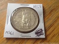 Obverse side of 1958 Canadian silver dollar coin showing the indigenous art eagle design, encased in white cardboard holder marked with year and grade.