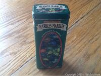 Front view of green rectangular tin labeled 'Marbles Marbles' showing colorful cat's eye marbles graphic.