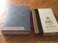 Two Bible boxes side by side on a wooden floor, one black with Holman label and one white with black spine and World Bible text