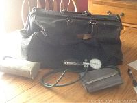 Photo showing the black leather vintage doctor's bag with medical items laid out including the blood pressure cuff and a rolled paper.