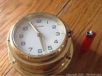 Front view of Forestville brass wall clock showing face, hands, and brand name with a red lighter for scale.