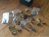 Overview of collection of souvenir enamel pins loosely arranged on wood surface, includes pins with Alaska, Victoria, Glacier Bay themes