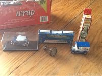 Lot of 5 small toys on wooden surface, including model cars, toy in packaging, flashlight, and boxed item