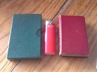 Two small books side by side with red cover book and green slipcase, lighter for size scale