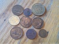 Full lot of nine coins arranged on wood surface showing varying sizes and designs including half penny ship-themed coins and other coins.