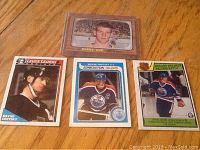 Overview photo showing all four hockey cards on wood surface including Bobby Orr card in protective case and three Wayne Gretzky cards