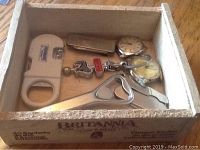 Wooden box containing various small miscellaneous items arranged including watches, keychains, tools, and magnifying device.
