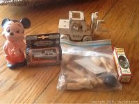 Photo of Mickey Mouse figure, Tonka toy truck, Motormax Mini Cooper model car, small boxed music box and ziplock bag of wooden figures on wooden floor.