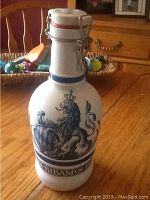 Photo showing front view of the ceramic bottle with lion crest and clasp lid against a wooden dining table.