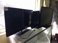 Three TVs side by side on glass display case, front view