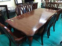 Full view of the rectangular wooden dining table surrounded by six chairs, showing the top surface, wood grain and finish.