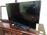 Front view of the Insignia 39-inch flatscreen TV on a wooden stand with remote control placed below the screen.
