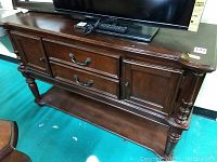 Front view showing wooden buffet with two drawers and two side cabinets with metal handles, topped with a TV and remotes (not included).