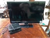 Front view of Dynex 32 inch flatscreen TV on a wooden table with two DVD players stacked in front.