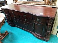 Front view of wooden credenza showing drawers and ornate carved details on corners and hardware.