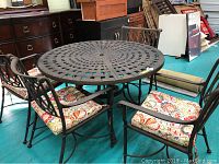 Overview of round metal patio table and four matching metal chairs with floral-pattern seat cushions.