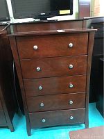 Front view of the wooden chest of drawers with five closed drawers and visible metal knobs.