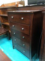 Frontal view of the dark wood chest of drawers with five drawers closed, showing overall condition.