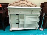 Front view of the white dresser showing three small drawers on top and two louvered sliding doors below.
