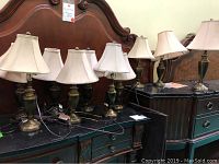 Ten table lamps arranged on a black surface, visible brass bases with beige shades, varying heights.