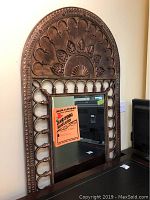 Full view of arched metal frame mirror leaning against wall with reflective glass and decorative top