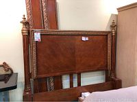 Full headboard leaning against wall showing carved frame, central veneer panels, and turned columns