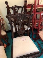 Front-facing view of two carved wooden chairs with upholstered cream seats placed upside down showing the carved backs and overall design.