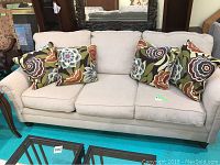 Front view of beige upholstered sofa with all five floral patterned pillows on it