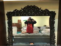 Front view of one ornate wall mirror with carved wood frame including floral and bird motifs reflecting a room with couches