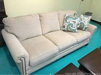 Front view of beige upholstered three-seat sofa with accent pillows