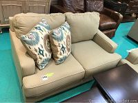 Front view of beige upholstered love seat with two patterned throw pillows on seat cushions.