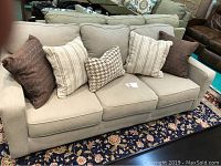 Front view of beige upholstered sofa with five pillows on floral rug