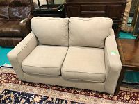 Front view of beige upholstered love seat on a patterned rug with two seat and two back cushions.